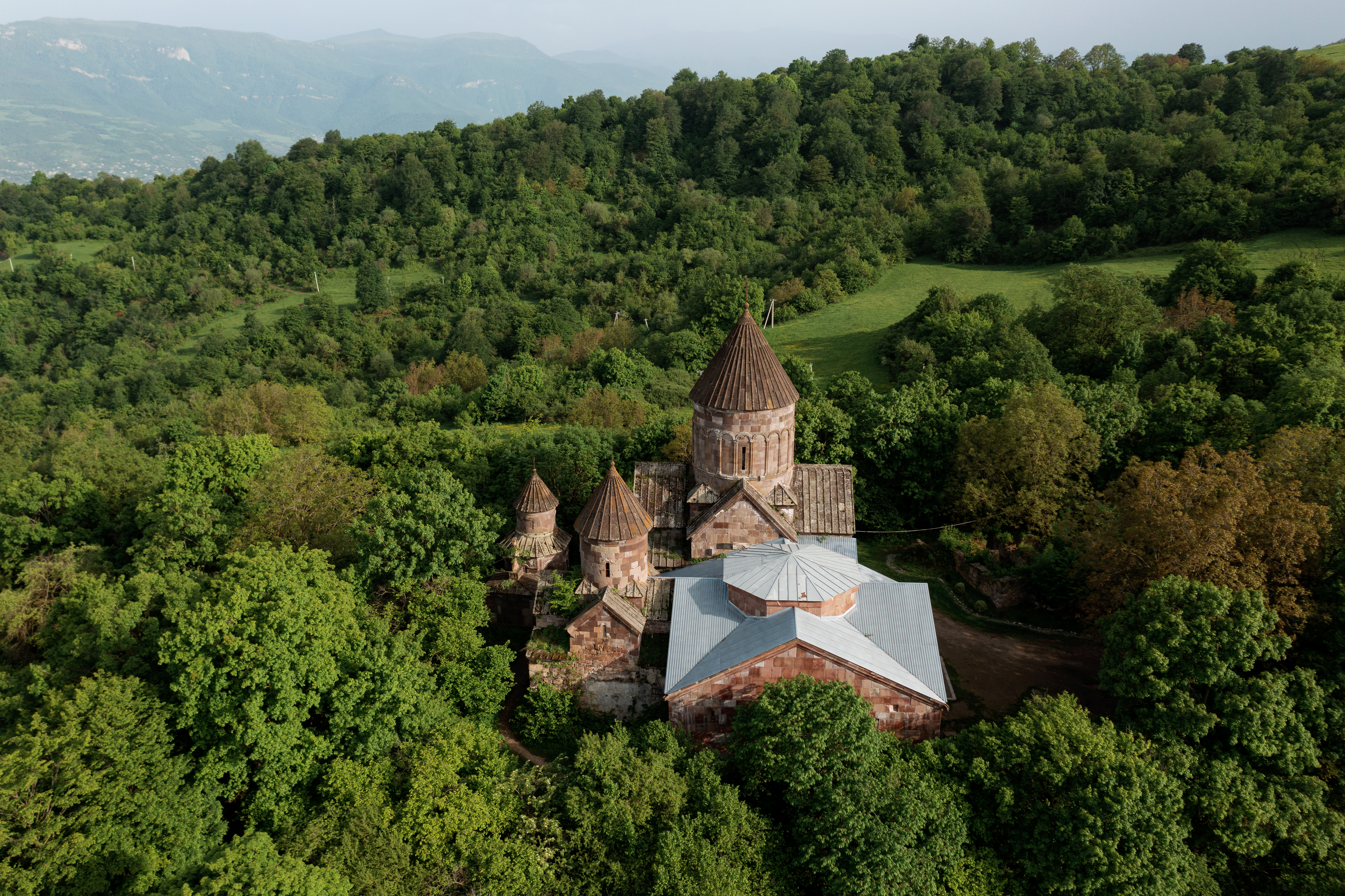 Aerial view of an ancient stone monastery nestled in lush Armenian forest