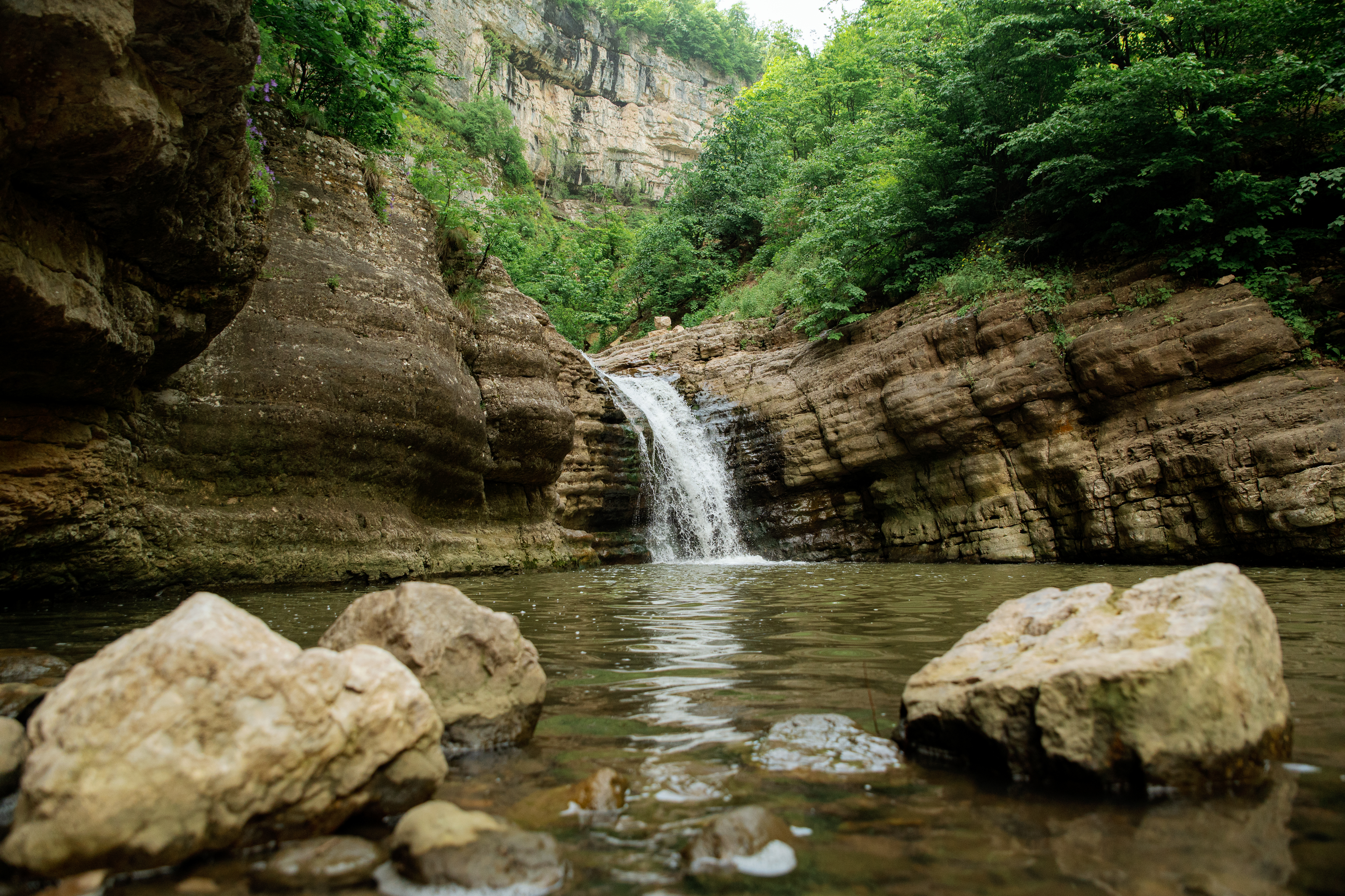 A waterfall cascading into a serene pool surrounded by layered limestone canyon walls